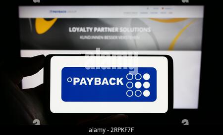 Persona che possiede un telefono cellulare con il logo della società tedesca Payback GmbH di gestione della fidelizzazione sullo schermo davanti alla pagina Web. Concentrarsi sul display del telefono. Foto Stock