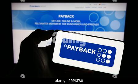 Persona che possiede il cellulare con il logo della società tedesca di gestione della fidelizzazione Payback GmbH sullo schermo davanti alla pagina Web. Concentrarsi sul display del telefono. Foto Stock