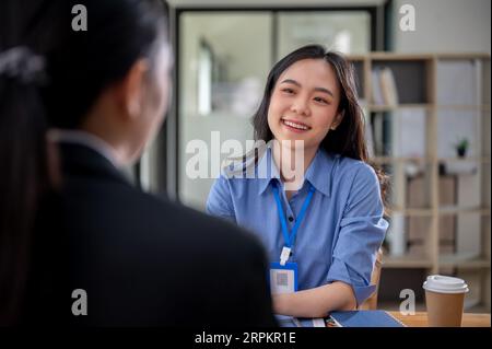 Una bella e amichevole reclutatrice asiatica di risorse umane sta intervistando un candidato in ufficio. Una giovane donna d'affari asiatica felice ama parlare con lui Foto Stock