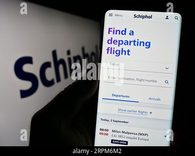 Persona in possesso di cellulare con pagina web della società aeroportuale olandese Royal Schiphol Group NV sullo schermo con logo. Concentrarsi sul centro del display del telefono. Foto Stock