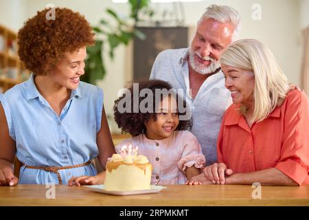 Famiglia multi-generazione che celebra il compleanno della nipote a casa con torta Foto Stock