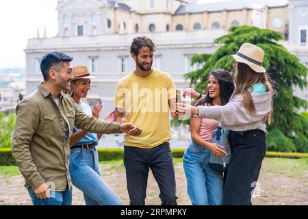 Gruppo multietnico di amici che festeggiano in un parco cittadino con birre. divertimento estivo, saluti al nuovo amico che è arrivato Foto Stock