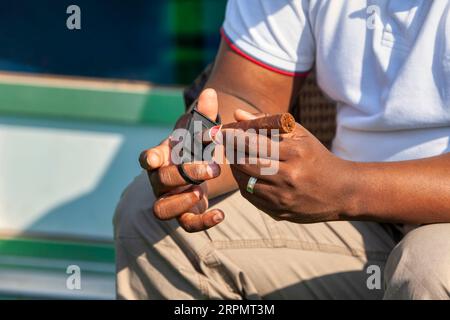 Un uomo d'affari afro-americano si trovava all'aperto usando un tagliaerba Guillotine per tagliare un sigaro di alta qualità Foto Stock