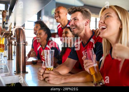 Gruppo multiculturale di amici che indossa le maglie della squadra nel bar dello sport per festeggiare la partita in TV Foto Stock