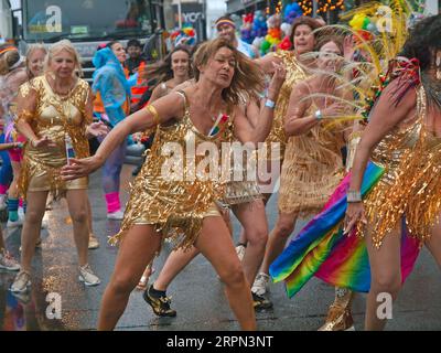 Donne in oro ballano sotto la pioggia al Brighton Pride 2023 Foto Stock