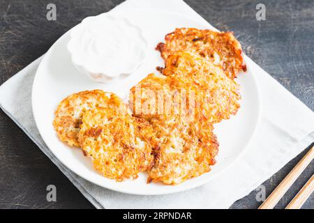 Frittelle di patate o latkes o draniki con panna acida. Cibo ucraino. Un piatto di patate grattugiato di Deruny o Draniki Foto Stock