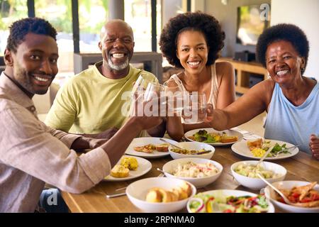 Ritratto della famiglia con genitori anziani e figli adulti intorno al tavolo a casa che fa la brindisi prima di mangiare Foto Stock