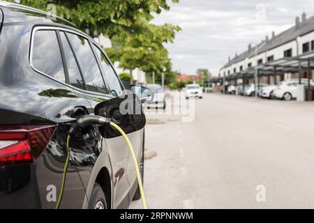 Auto elettrica con cavo di ricarica collegato a un punto di ricarica per veicoli elettrici nel parcheggio della città. Concetto di energia rinnovabile. Foto Stock