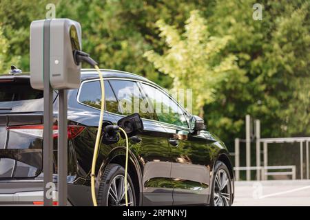 Auto elettrica con cavo di ricarica collegato a un punto di ricarica per veicoli elettrici nel parcheggio della città. Concetto di energia rinnovabile. Foto Stock