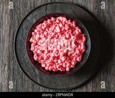 insalata cremosa di mirtilli rossi con mini marshmallow, mela fresca e noci pecan in ciotola nera su tavolo di legno scuro, ricetta americana, vista orizzontale da a. Foto Stock