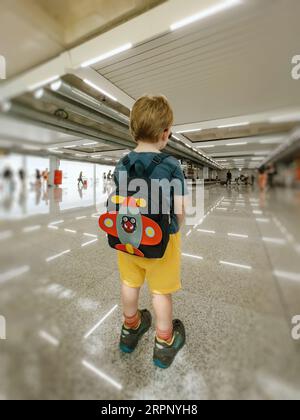 Un bambino perduto in un aeroporto, da solo e triste, guarda fuori dalla finestra degli aerei, desideroso di un'avventura. Foto Stock