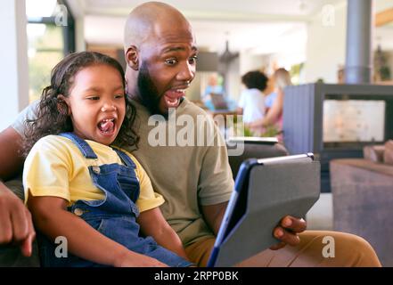 Padre e figlia che utilizzano un tablet digitale a casa con famiglia di generazioni multiple in background Foto Stock