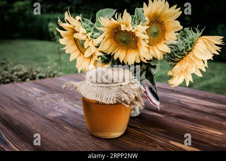 Bouquet di girasoli freschi e miele di girasoli in vasetti di vetro. Prodotti dell'apicoltura durante la raccolta del miele e la fioritura Foto Stock