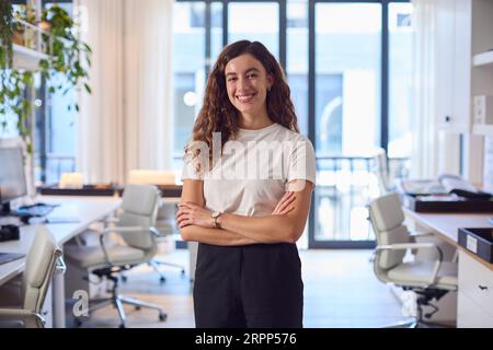 Ritratto di giovane donna d'affari sorridente in piedi nell'ufficio moderno Foto Stock
