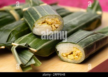 Lemper Ayam intero e tagliato a metà avvolto in foglie di banana, uno spuntino salato indonesiano a base di riso glutinoso ripieno con pollo tagliato a pezzetti stagionato Foto Stock