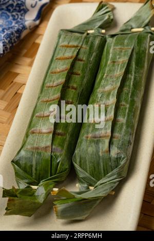 Lemper Ayam intero alla griglia avvolto in foglie di banana, uno spuntino salato indonesiano a base di riso glutinoso ripieno di pollo sminuzzato condito da vicino Foto Stock