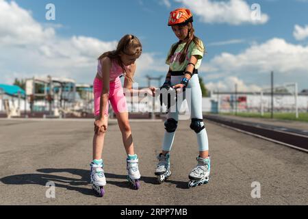 pattinaggio a rotelle per scolaresche. ragazze in ginocchiere con dispositivi di protezione e una ragazza con un trauma sulla pelle dopo una caduta Foto Stock