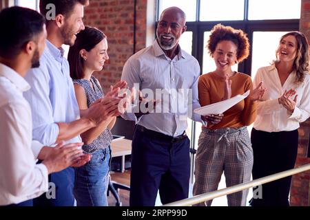 Colleghi che applaudono l'incontro di un uomo d'affari che conduce la riunione del team in un ufficio multiculturale molto impegnato Foto Stock