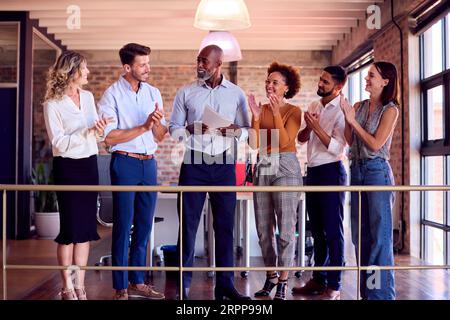 Colleghi che applaudono l'incontro di un uomo d'affari che conduce la riunione del team in un ufficio multiculturale molto impegnato Foto Stock