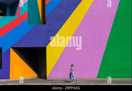 La donna passeggia davanti alla Towner Art Gallery con le colorate opere d'arte Dance Diagonal dell'artista tedesco Lothar Götz a Eastbourne, East Sussex, Regno Unito, a settembre Foto Stock