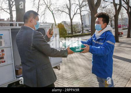 200314 -- PECHINO, 14 marzo 2020 -- Un cliente scatta una foto per li Jie R mentre riceve il suo pacco a Pechino, capitale della Cina, 12 marzo 2020. Li è popolare dopo aver partecipato a una conferenza stampa mostrata in televisione. Li Jie, un addetto alla consegna di ZTO Express, lavora nel settore della consegna espressa da 11 anni. Invece di tornare a casa a Xiong An New area, nella provincia di Hebei, nella Cina settentrionale, è rimasto a Pechino e ha lavorato durante l'ultima festa del Festival di Primavera. Dopo lo scoppio della COVID-19, le persone preferiscono rimanere a casa per prevenire la diffusione del coronavirus nel frattempo gli ordini online sono incl Foto Stock