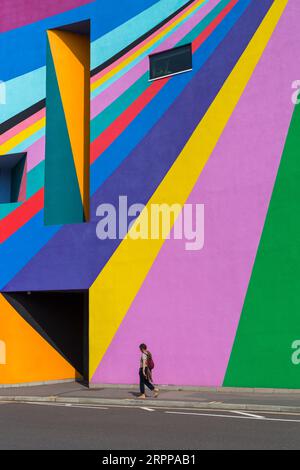 La donna passeggia davanti alla Towner Art Gallery con le colorate opere d'arte Dance Diagonal dell'artista tedesco Lothar Götz a Eastbourne, East Sussex, Regno Unito, a settembre Foto Stock