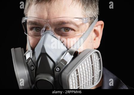 Ritratto di un uomo in un respiratore protettivo, una maschera con filtri per polvere e gas, su sfondo nero. Foto Stock