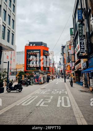 Un'idilliaca e stretta strada acciottolata costeggiata da edifici color pastello e persone che viaggiano in moto lungo il percorso Foto Stock