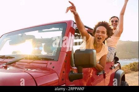Gruppo di amiche che ridono si divertono in un'auto a tetto aperto durante il viaggio in auto Foto Stock