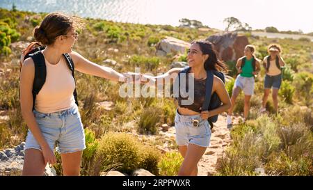 Gruppo di amiche femminili con zaini che si aiutano a vicenda nelle escursioni in campagna lungo Coastal Path Foto Stock