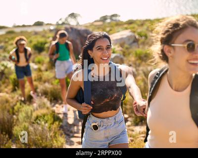 Gruppo di amiche femminili con zaini che si aiutano a vicenda nelle escursioni in campagna lungo Coastal Path Foto Stock