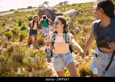 Gruppo di amiche femminili con zaini che si aiutano a vicenda nelle escursioni in campagna lungo Coastal Path Foto Stock