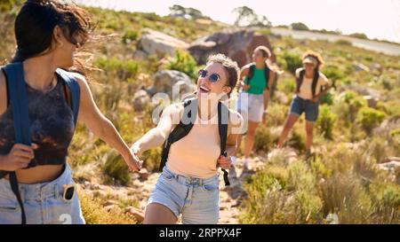 Gruppo di amiche femminili con zaini che si aiutano a vicenda nelle escursioni in campagna lungo Coastal Path Foto Stock