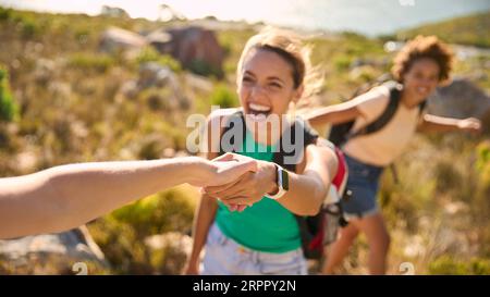 Gruppo di amiche femminili con zaini che si aiutano a vicenda nelle escursioni in campagna lungo Coastal Path Foto Stock