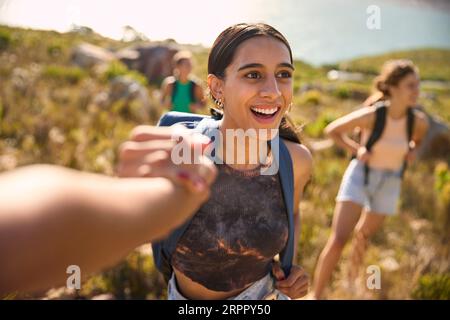 Gruppo di amiche femminili con zaini che si aiutano a vicenda nelle escursioni in campagna lungo Coastal Path Foto Stock