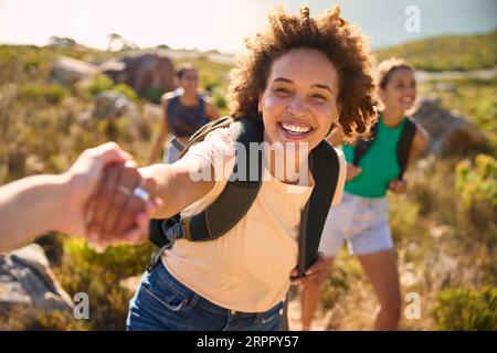 Gruppo di amiche femminili con zaini che si aiutano a vicenda nelle escursioni in campagna lungo Coastal Path Foto Stock