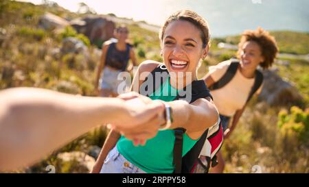 Gruppo di amiche femminili con zaini che si aiutano a vicenda nelle escursioni in campagna lungo Coastal Path Foto Stock