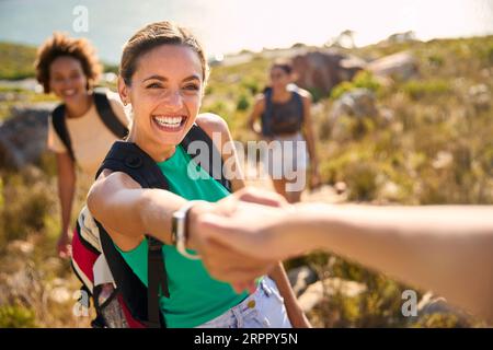 Gruppo di amiche femminili con zaini che si aiutano a vicenda nelle escursioni in campagna lungo Coastal Path Foto Stock