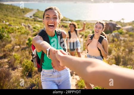 Gruppo di amiche femminili con zaini che si aiutano a vicenda nelle escursioni in campagna lungo Coastal Path Foto Stock