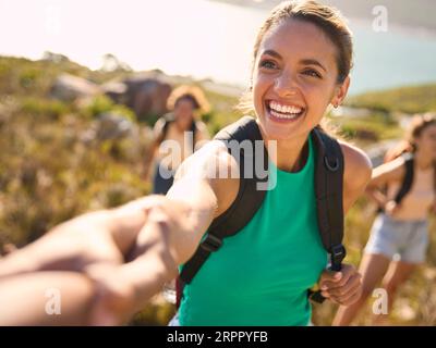 Gruppo di amiche femminili con zaini che si aiutano a vicenda nelle escursioni in campagna lungo Coastal Path Foto Stock