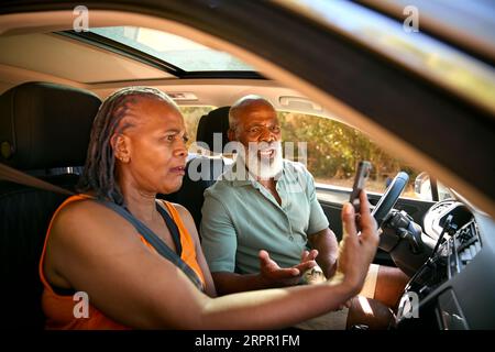 Coppia anziana in auto che discute delle indicazioni sul navigatore satellitare GPS sul telefono cellulare durante la gita di un giorno Foto Stock