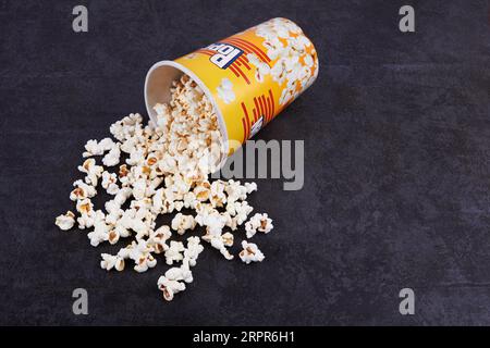 Popcorn sparsi dal secchio giallo su sfondo scuro Foto Stock