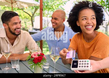 Donna che effettua pagamenti senza contatto presso un bar o un ristorante all'aperto con carta di credito o di debito Foto Stock