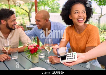 Donna che paga il conto al bar o ristorante all'aperto utilizzando l'app Contactless sul telefono cellulare Foto Stock