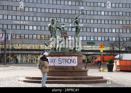 200331 -- HELSINKI, 31 marzo 2020 -- Un cittadino si ferma presso la famosa scultura cittadina Three Smiths che è stata indossata su maschere facciali, a Helsinki, Finlandia, 31 marzo 2020. A partire da lunedì, i casi di coronavirus in Finlandia erano a 1.313 con 13 morti, secondo l'Istituto finlandese per la salute e il benessere THL. FINLANDIA-HELSINKI-COVID-19 ZhuxHaochen PUBLICATIONxNOTxINxCHN Foto Stock