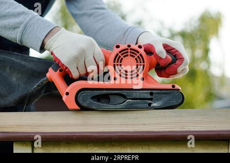 Primo piano della falegnameria utilizzando la levigatrice elettrica per la levigatura della tavola Foto Stock