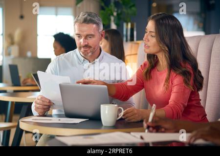 Donna d'affari matura e uomo d'affari che lavora su un notebook nell'area salotto informale dell'ufficio moderno Foto Stock