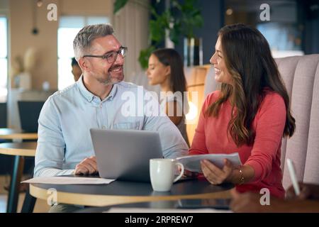 Donna d'affari matura e uomo d'affari che lavora su un notebook nell'area salotto informale dell'ufficio moderno Foto Stock