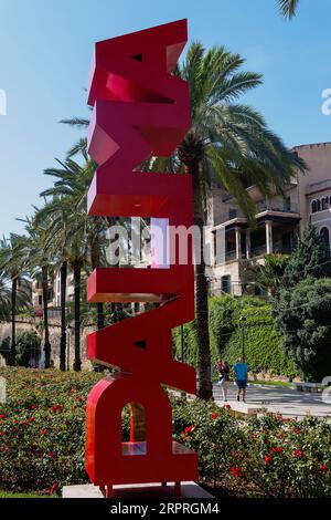 Spagna, Isole Baleari, Maiorca, Palma di Maiorca. Scultura Palma. Cartello rosso Palma sul Paseo Sagrera o Passeig de Sagrera in catalano, una tranquilla passeggiata sul lungomare. Foto Stock