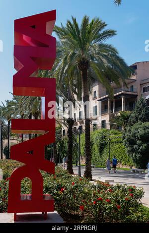 Spagna, Isole Baleari, Maiorca, Palma di Maiorca. Scultura Palma. Cartello rosso Palma sul Paseo Sagrera o Passeig de Sagrera in catalano, una tranquilla passeggiata sul lungomare. Foto Stock